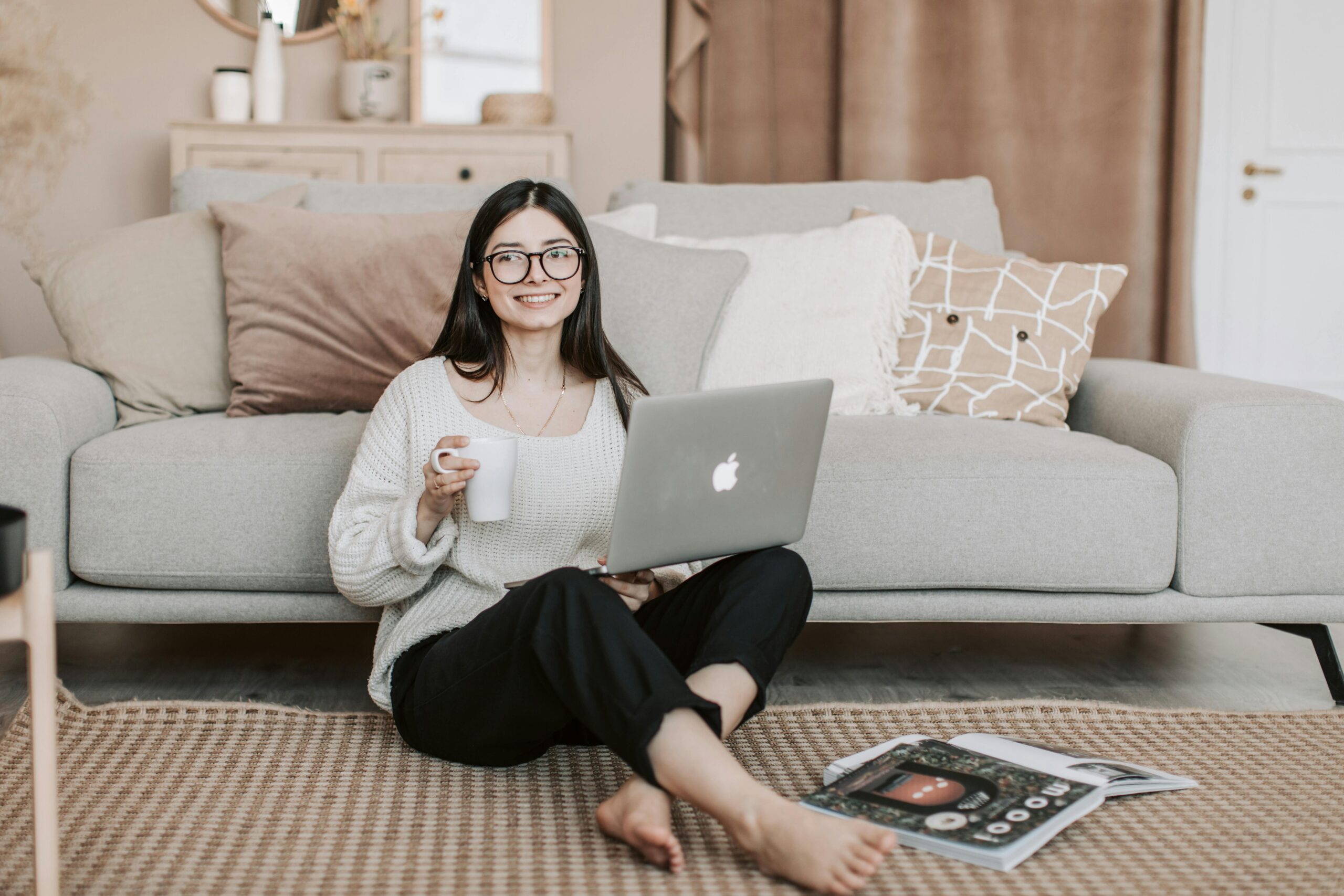Mujer feliz disfrutando de un café mientras usa una laptop en una sala acogedora.